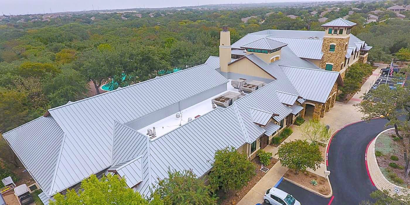 A commercial campus with light gray metal roofs among the trees