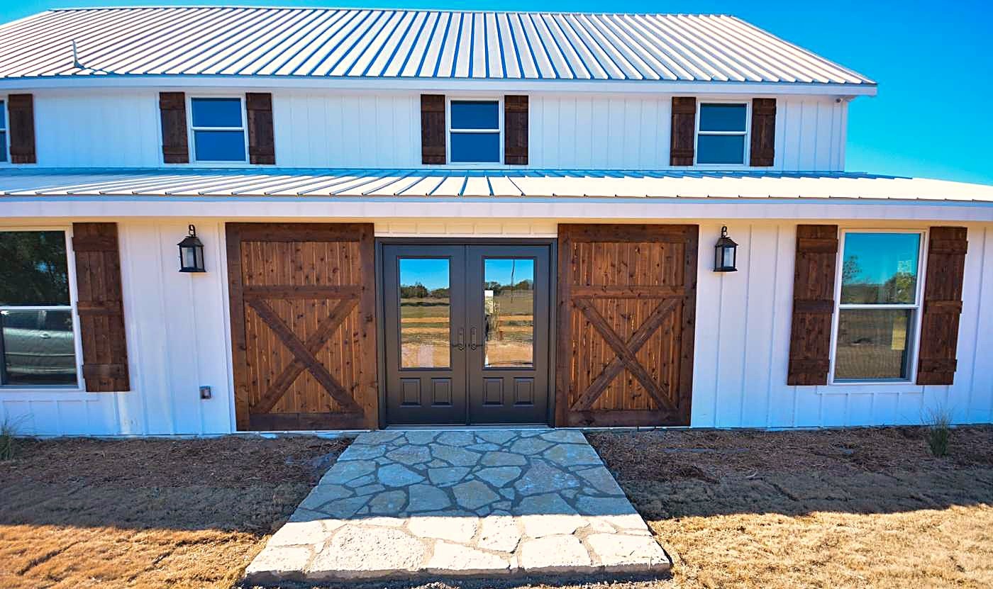 A white farmhouse with a standing-seam metal roof and barn-style doors