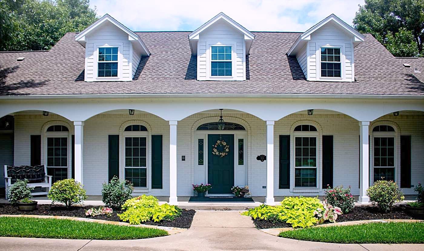 A white home with three dormers and a long front porch under a gray roof